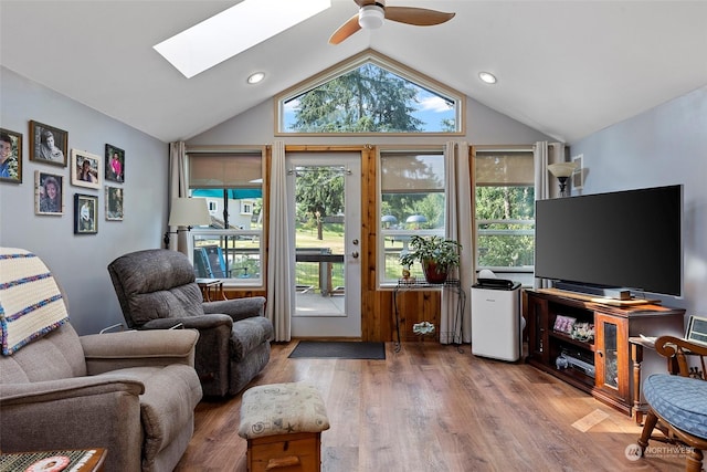 living room with ceiling fan, wood-type flooring, and vaulted ceiling with skylight