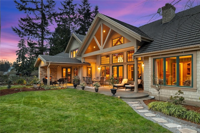 back house at dusk with a patio and a lawn