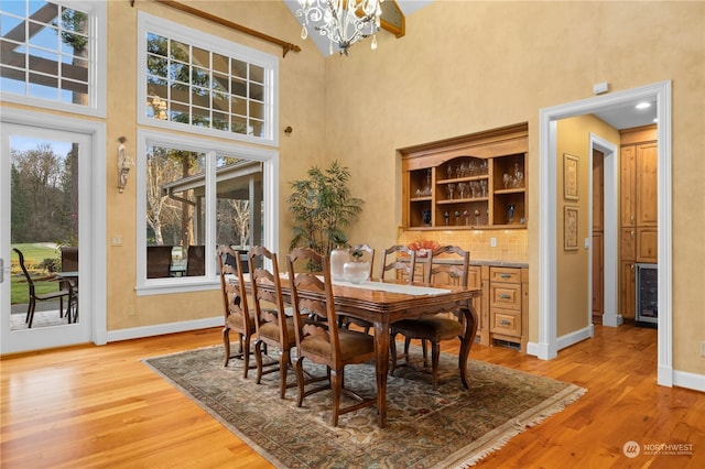 dining space featuring an inviting chandelier, a high ceiling, light hardwood / wood-style flooring, and wine cooler