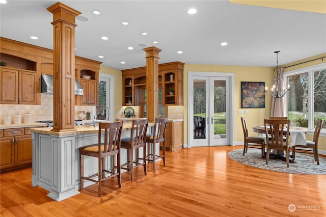 kitchen featuring pendant lighting, wall chimney range hood, a kitchen breakfast bar, a kitchen island, and ornate columns