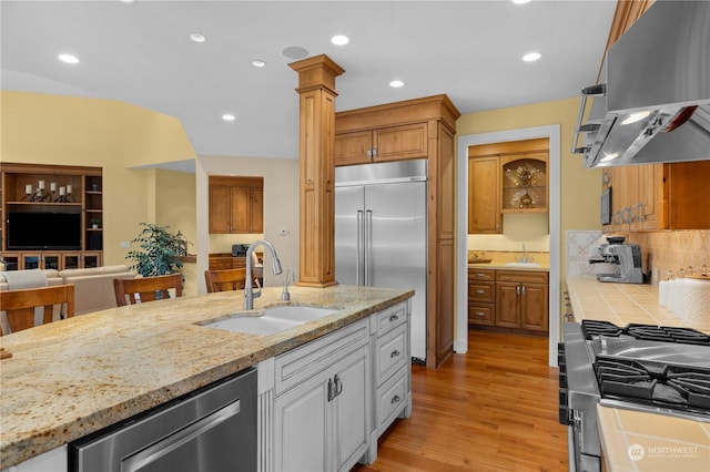 kitchen featuring extractor fan, sink, ornate columns, stainless steel appliances, and light stone countertops