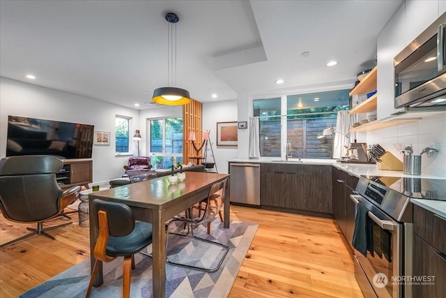 kitchen with tasteful backsplash, decorative light fixtures, dark brown cabinets, appliances with stainless steel finishes, and light hardwood / wood-style floors