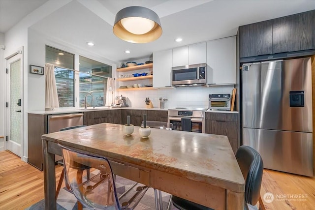 kitchen with sink, light wood-type flooring, stainless steel appliances, decorative backsplash, and white cabinets