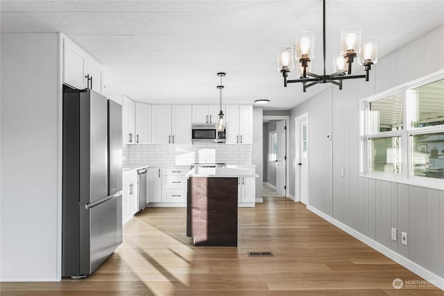 kitchen with pendant lighting, white cabinetry, a center island, stainless steel appliances, and light hardwood / wood-style flooring