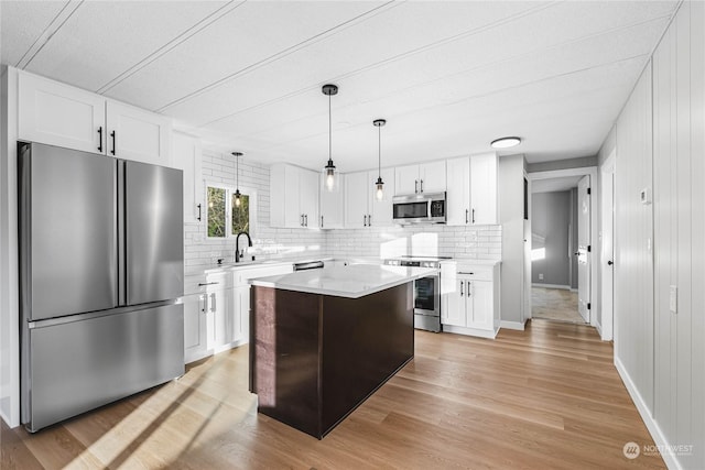 kitchen with appliances with stainless steel finishes, white cabinetry, hanging light fixtures, a center island, and light hardwood / wood-style flooring