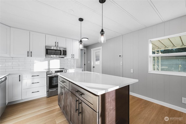 kitchen with pendant lighting, appliances with stainless steel finishes, white cabinetry, a center island, and light hardwood / wood-style floors