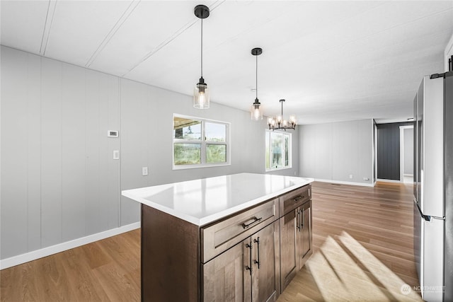 kitchen with decorative light fixtures, a center island, dark brown cabinets, light hardwood / wood-style flooring, and stainless steel refrigerator