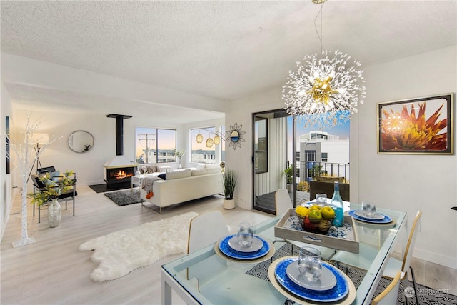 dining area featuring a notable chandelier, a wood stove, a textured ceiling, and light hardwood / wood-style floors