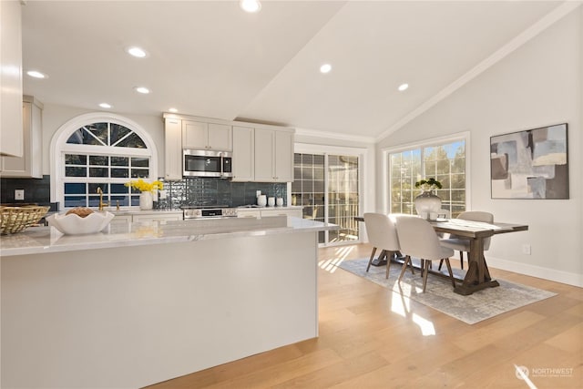 kitchen featuring lofted ceiling, light stone counters, light wood-type flooring, appliances with stainless steel finishes, and white cabinets