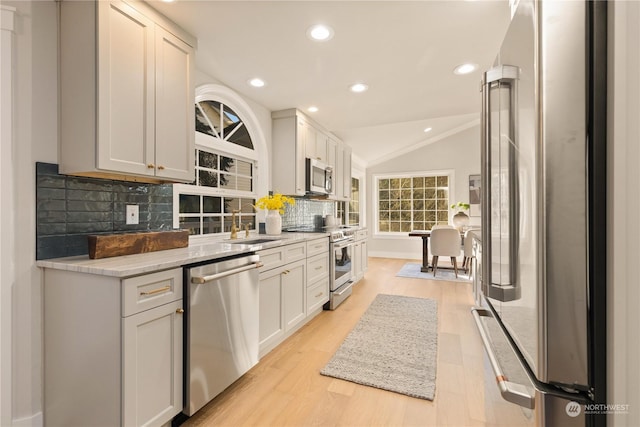 kitchen with light stone counters, white cabinets, stainless steel appliances, light hardwood / wood-style floors, and backsplash