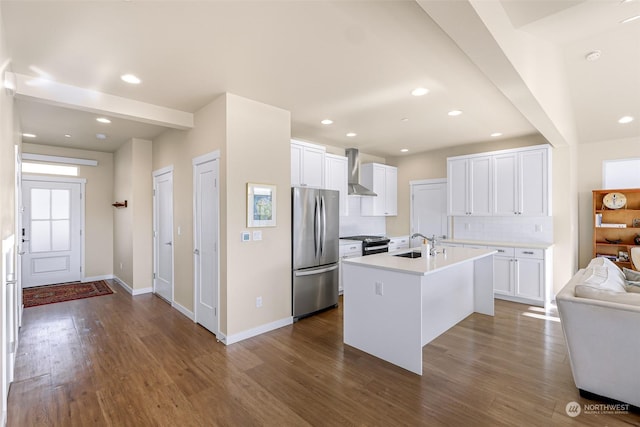 kitchen with sink, white cabinets, a kitchen island with sink, stainless steel appliances, and wall chimney range hood