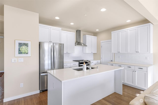 kitchen with white cabinetry, appliances with stainless steel finishes, a kitchen island with sink, and wall chimney range hood