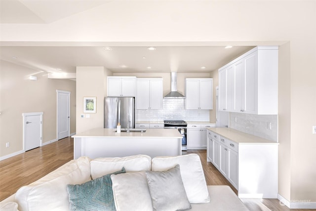 kitchen with stainless steel appliances, wall chimney range hood, a center island with sink, and white cabinetry