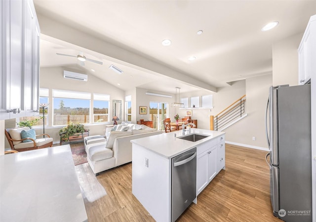 kitchen with sink, appliances with stainless steel finishes, white cabinetry, hanging light fixtures, and an island with sink