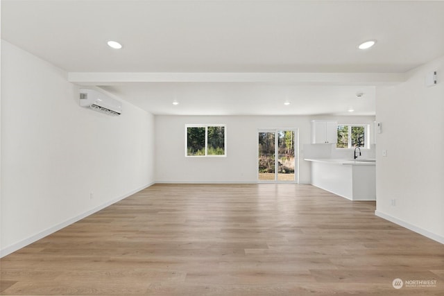 unfurnished living room featuring sink, a wealth of natural light, light hardwood / wood-style floors, and a wall mounted AC