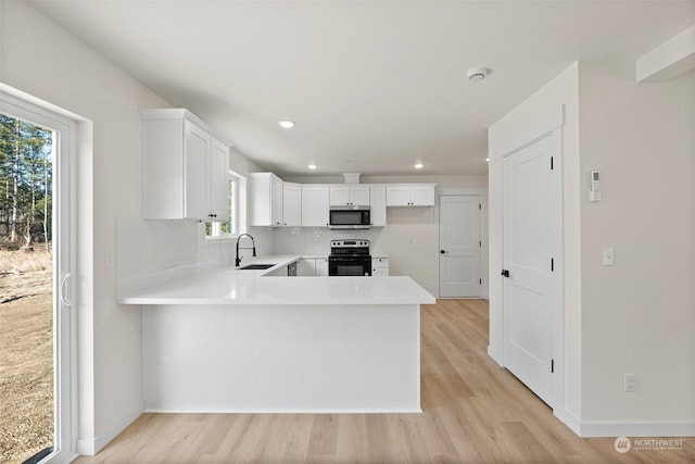 kitchen with black electric range oven, sink, white cabinetry, tasteful backsplash, and kitchen peninsula