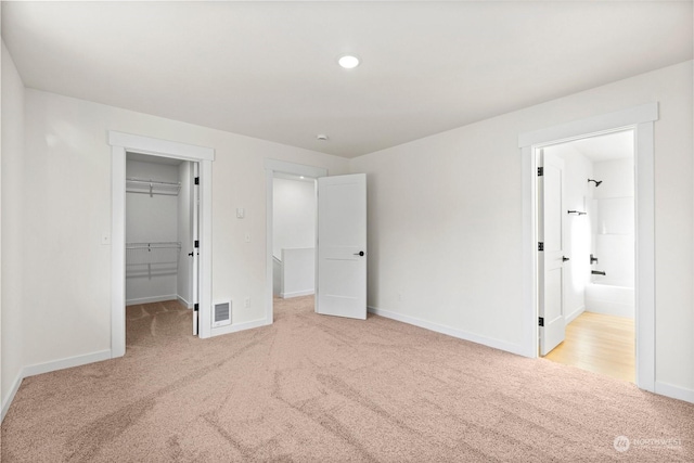 unfurnished bedroom with a spacious closet, light colored carpet, ensuite bath, and a closet