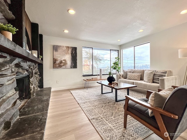 living room featuring a stone fireplace, light hardwood / wood-style floors, and a textured ceiling