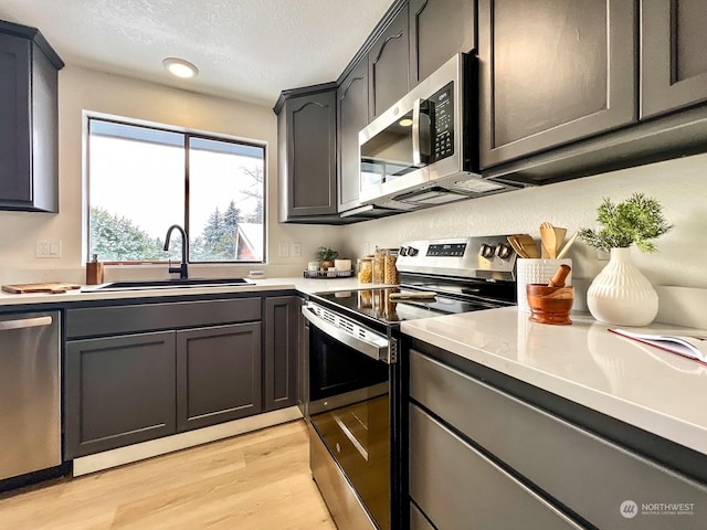 kitchen with appliances with stainless steel finishes, light hardwood / wood-style floors, sink, and a textured ceiling