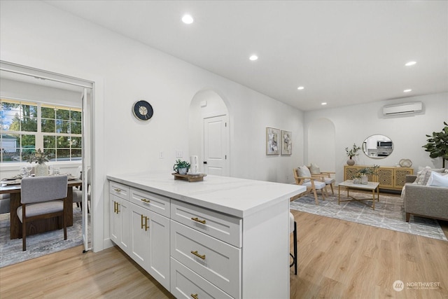 kitchen with a breakfast bar area, light stone counters, a wall mounted air conditioner, white cabinets, and light wood-type flooring