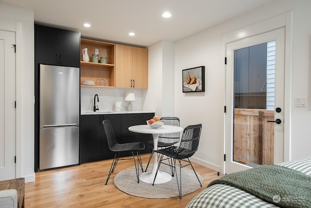 interior space featuring sink, tasteful backsplash, light wood-type flooring, light brown cabinets, and stainless steel fridge