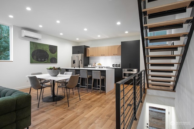 kitchen featuring light brown cabinets, appliances with stainless steel finishes, a kitchen breakfast bar, an island with sink, and a wall unit AC