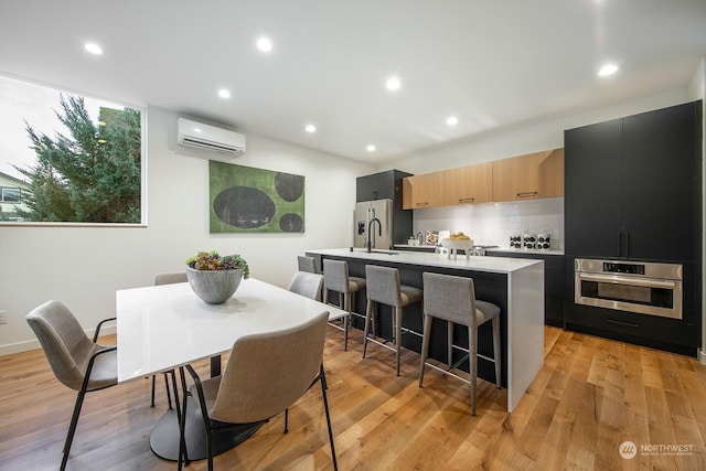 kitchen with a kitchen bar, light brown cabinetry, a center island with sink, appliances with stainless steel finishes, and a wall unit AC