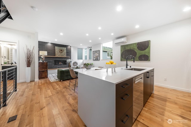 kitchen featuring a fireplace, sink, stainless steel dishwasher, light hardwood / wood-style floors, and a center island with sink