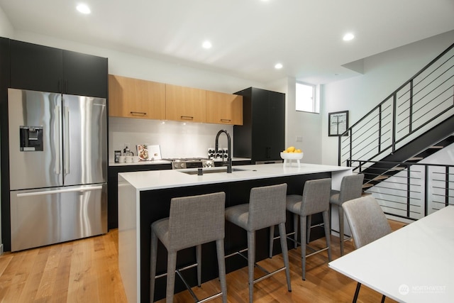 kitchen with stainless steel fridge with ice dispenser, a kitchen breakfast bar, an island with sink, and light wood-type flooring