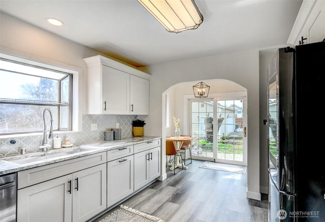 kitchen with dishwasher, decorative backsplash, freestanding refrigerator, arched walkways, and a sink