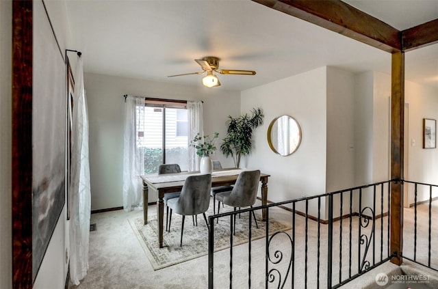 carpeted dining area featuring beamed ceiling, baseboards, and a ceiling fan