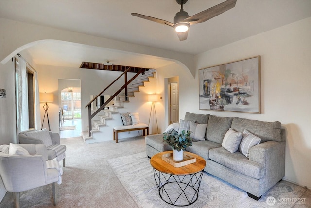 carpeted living area with stairs, a ceiling fan, and arched walkways