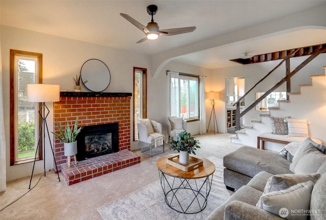 living room with stairway, a ceiling fan, a fireplace, and carpet