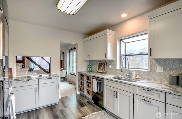 kitchen featuring dark wood-style flooring, a sink, white cabinets, dishwasher, and tasteful backsplash