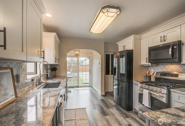 kitchen with a sink, gas stove, arched walkways, light stone countertops, and black refrigerator with ice dispenser