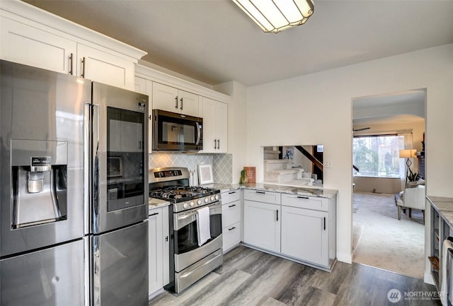 kitchen featuring light stone counters, tasteful backsplash, white cabinetry, stainless steel appliances, and light wood-style floors