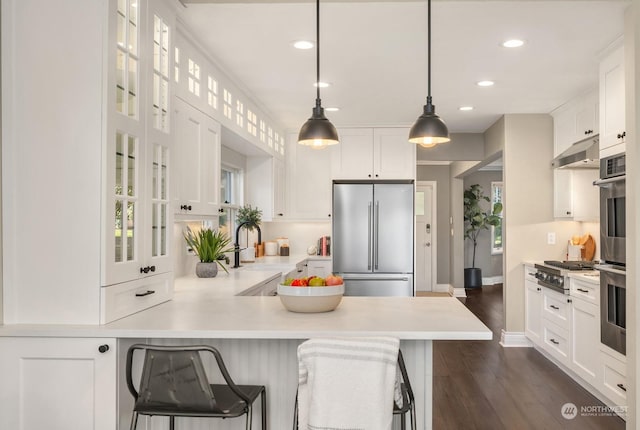 kitchen with a kitchen bar, appliances with stainless steel finishes, kitchen peninsula, pendant lighting, and white cabinets