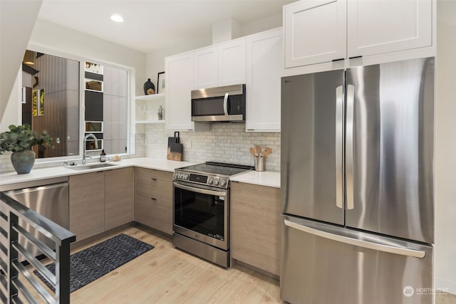 kitchen with tasteful backsplash, white cabinetry, sink, stainless steel appliances, and light wood-type flooring