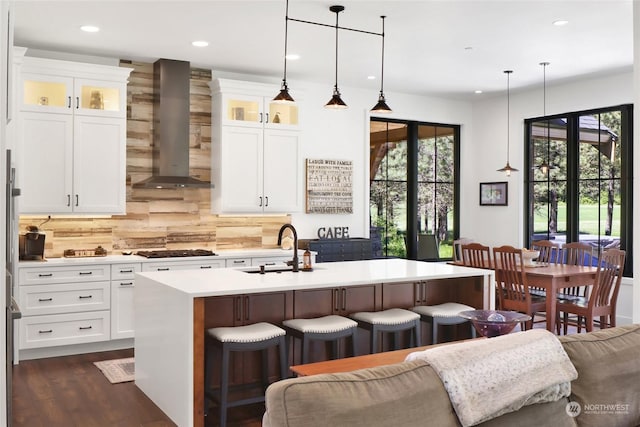 kitchen featuring sink, hanging light fixtures, an island with sink, and wall chimney exhaust hood