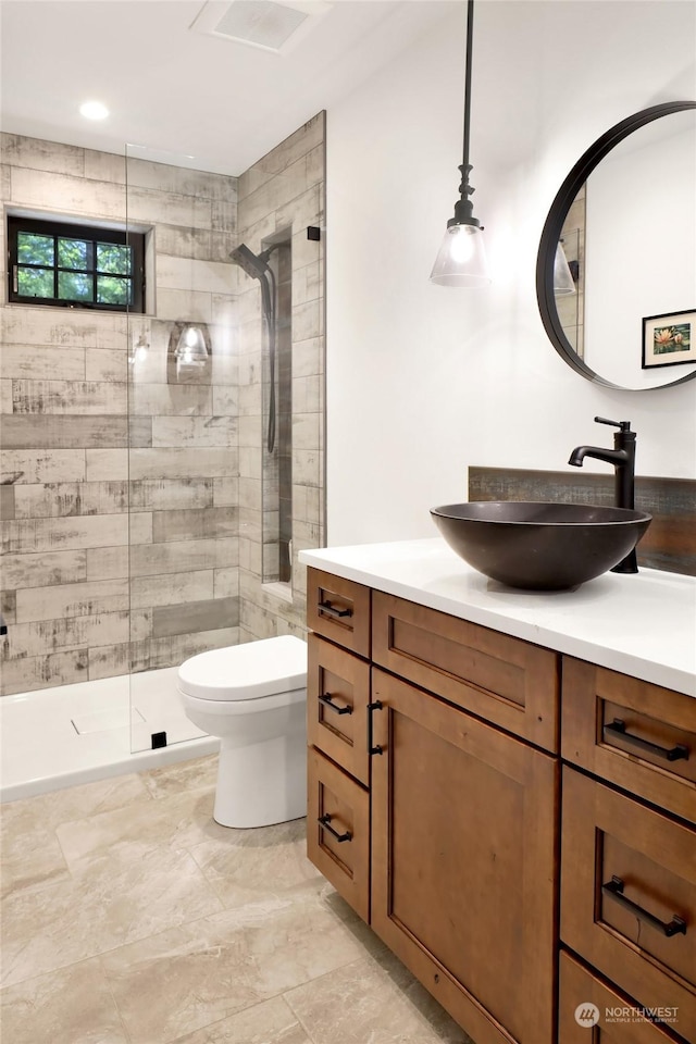 bathroom with tiled shower, vanity, and toilet