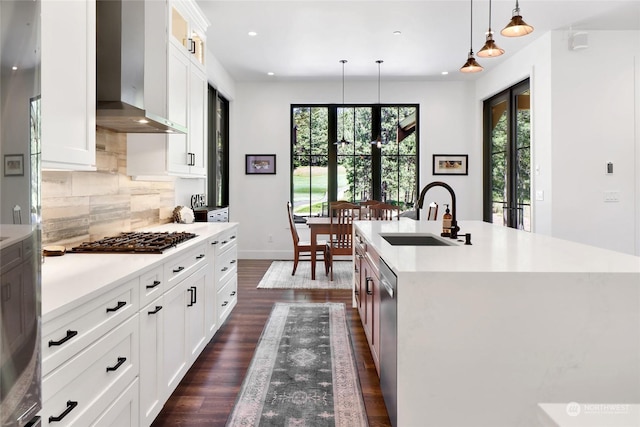 kitchen featuring wall chimney exhaust hood, sink, white cabinetry, an island with sink, and pendant lighting