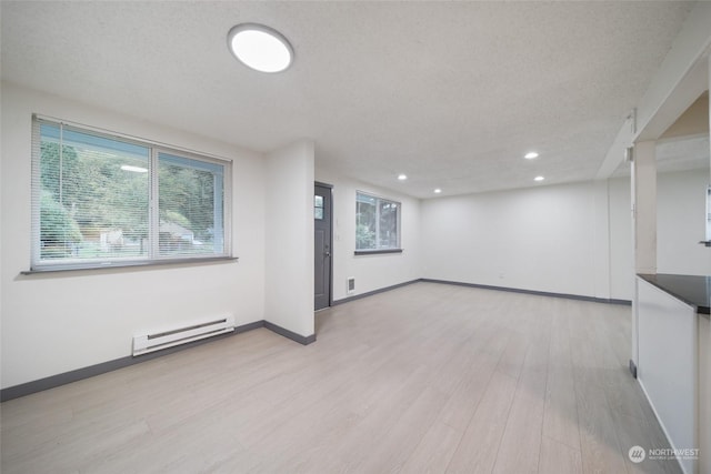 interior space with a textured ceiling, baseboard heating, and light hardwood / wood-style floors