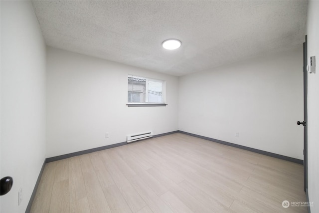 empty room with a textured ceiling, baseboard heating, and light hardwood / wood-style floors