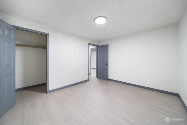 unfurnished bedroom with a textured ceiling, light hardwood / wood-style floors, and a closet