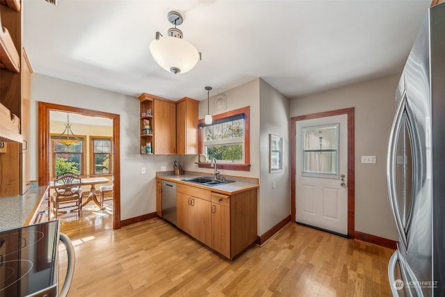 kitchen with stainless steel appliances, sink, pendant lighting, and light hardwood / wood-style floors