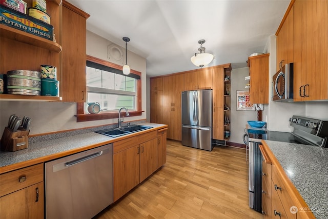 kitchen with appliances with stainless steel finishes, sink, pendant lighting, and light hardwood / wood-style flooring