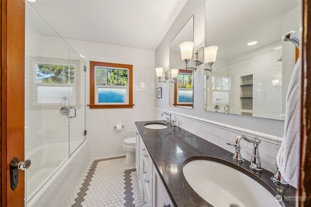 full bathroom featuring tile patterned floors, toilet, shower / bath combination with glass door, tile walls, and vanity