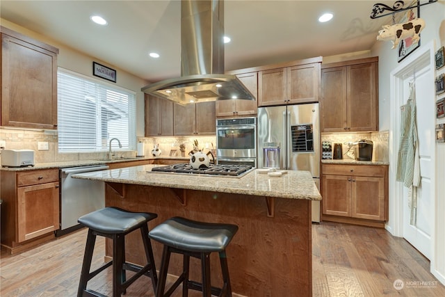 kitchen featuring light stone counters, a center island, island exhaust hood, stainless steel appliances, and light hardwood / wood-style floors