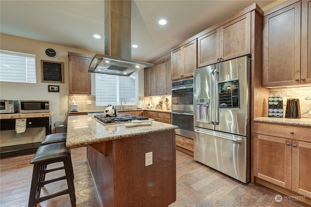 kitchen with appliances with stainless steel finishes, a breakfast bar, island exhaust hood, a center island, and light stone countertops