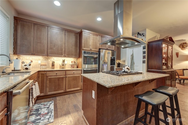 kitchen with sink, appliances with stainless steel finishes, a kitchen breakfast bar, light hardwood / wood-style floors, and island exhaust hood